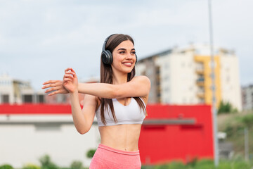 Athletic young woman with towel smiling and streaching. Young sporty woman training. Woman Doing Workout Exercises On Street . Fit girl streaching before active fitness training