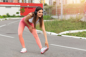 Woman Listening Music, Doing Workout Exercises On Street. Beautiful Athletic Fit Girl In Bright Sports Clothing Stretching Her Legs And Relaxing After Fitness Training On Street. High Quality Image
