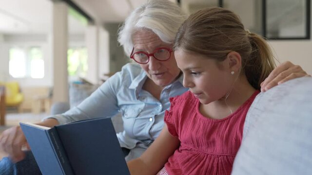 Grandmother with grandkid reading book in sofa