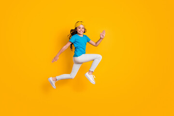 Fototapeta na wymiar Full body profile photo of funny little lady jumping high good mood cheerful jogging competition race wear casual blue t-shirt headband trousers shoes isolated yellow color background