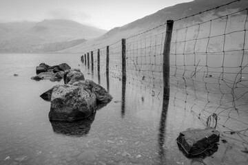 Black and white landscape of lake, with farmers fence leading into the water. Flooded landscape, natural beauty.