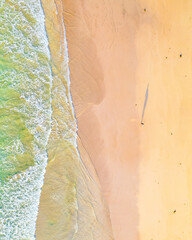 Top down aerial view of a beach with waves, rocks and sand.