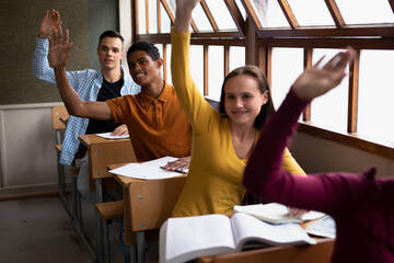 Front view of students raising their hands in class