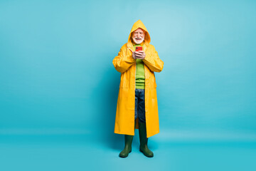 Full length body size view of his he nice cheerful cheery grey-haired man wearing long yellow topcoat using cell chatting free time isolated on bright vivid shine vibrant blue color background
