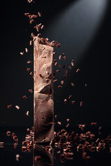 Piece of dark chocolate and falling chocolate crumbs.