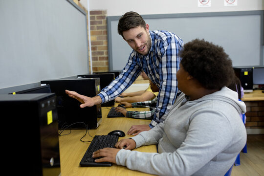 Side view of teacher helping student on computer