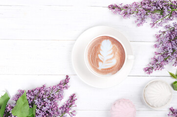 Lilac, coffee with latte art and marshmallow on white wooden table. Romantic morning. Flat lay