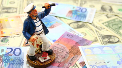 Small sailor on international paper money, observing, searching for new directions in economy,...