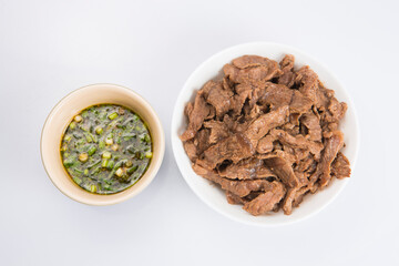 isolated close up flat lay top view shot of a bowl of sliced beef fillet pieces and a cup of Vietnamese Nuoc Cham dipping sauce on a white background