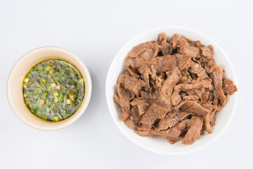 isolated close up flat lay top view shot of a bowl of sliced beef fillet pieces and a cup of Vietnamese Nuoc Cham dipping sauce on a white background