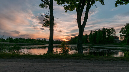 Obraz premium image with a beautiful colorful sunset over the lake, in the foreground the contours of trees and grass, Lielais Ansis, Rubene, Latvia