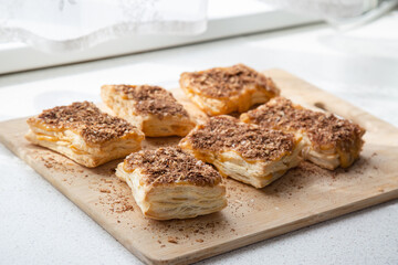 a few of baked square pieces of chocolate and caramel puff pastry cake on a wooden cutting board on table, white background. selective focus