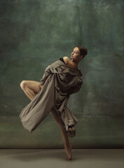 Fototapeta na wymiar Warm. Graceful classic ballerina dancing, posing isolated on dark studio background. Stylish trench coat. Grace, movement, action and motion concept. Looks weightless, flexible. Fashionable, style.