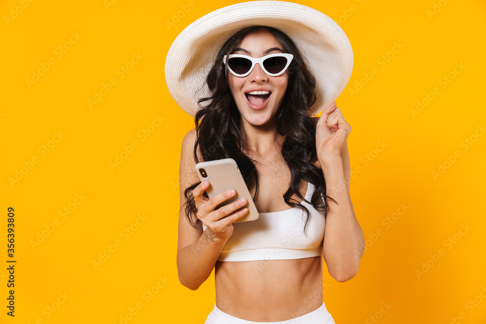 Wall mural image of amazed woman making winner gesture and using cellphone