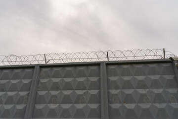 gray concrete wall with barbed wire against the background of a gray nondescript sky