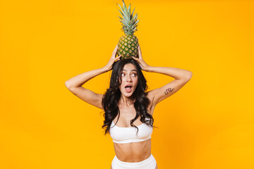 Image of surprised brunette woman holding pineapple on her head