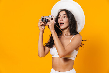 Image of focused beautiful woman in swimsuit and hat using retro camera