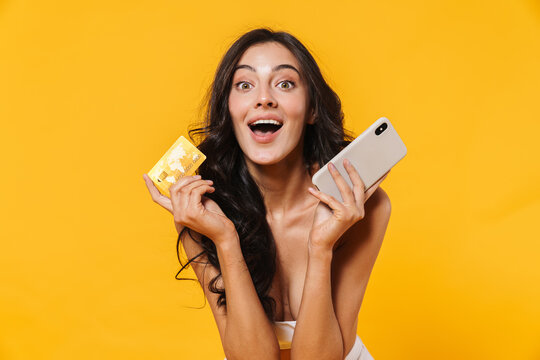 Image of excited woman in swimsuit holding credit card and cellphone