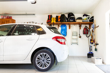 Home suburban car garage interior with wooden shelf , tools and equipment stuff storage warehouse on white wall indoors. Vehicle parked at house parking background - obrazy, fototapety, plakaty