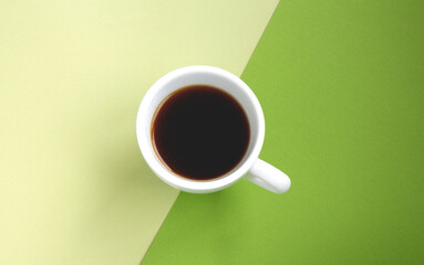 Black coffee in a white cup on a green background divided on two parts. Selective focus. Top view