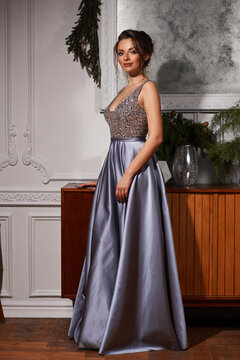 Young beautiful pretty caucasian woman with brown hair and makeup wearing elegant evening dress and posing in interior. Fashion portrait.