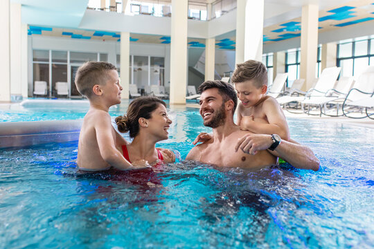 Smiling family of four having fun and relaxing in indoor swimming pool at hotel resort.