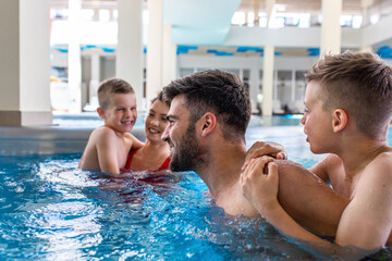 Smiling family of four having fun and relaxing in indoor swimming pool at hotel resort.