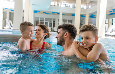 Smiling family of four having fun and relaxing in indoor swimming pool at hotel resort.