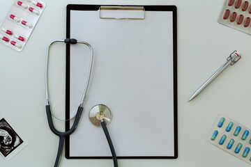 doctor's desktop with tablet with a sheet of paper for notes next to a statoscope pen and pills in blisters