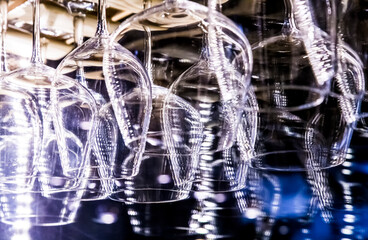 Transparent wine glasses hang down in the bar or restaurant or cafe. Close-up. Selective focus. Abstract background.