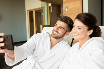 Fototapeta premium Smiling couple in bathrobe relaxing in spa center at hotel resort and making selfie.