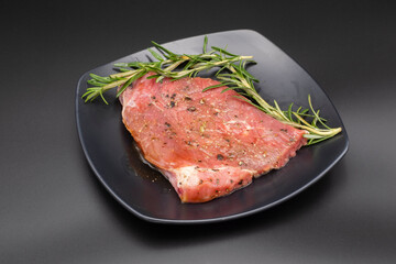 Raw beef with rosemary in black dish on black background, copyspace for you design.