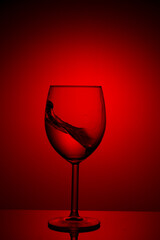 Fototapeta na wymiar A splash of red wine in a glass on a red background