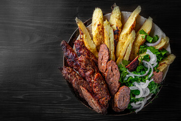 cut Lulia kebab with potato in plate on black wooden table background