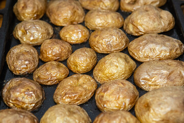 Tasty baked hot potatoes with peel on the platter, removed from the oven, close-up
