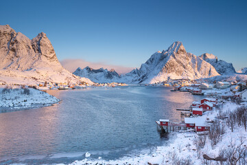 Serene fishing village on the shore in the north of Norway. The town covered with white fluffy snow in the beautiful winter while the morning sun light shining on the mountains, cliff, and sea. 