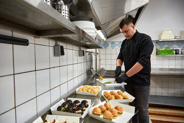 Young chef cook in black tunic prepares catering snacks.