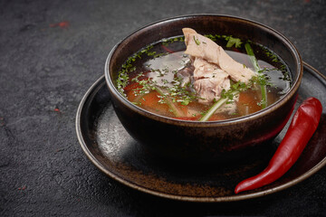 Chicken soup with vegetables in black bowl on black background