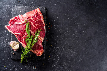 Cooking meat background. Raw aged beef t-bone steak, with spices and herbs for cooking on a gray...