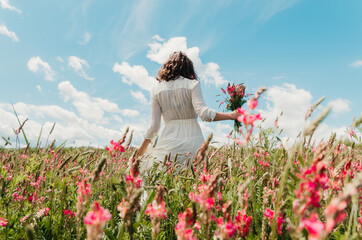 Back view woman holding wildflower bouquet doing graceful stroll through a blossoming flower field