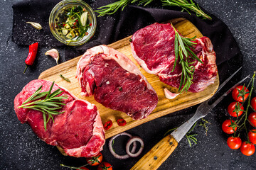 Raw meat, beef steak on cutting board with rosemary and spices, black background, top view copy space