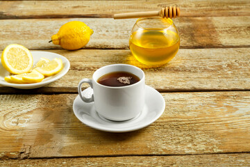 White cup with tea with lemon and honey on the table.