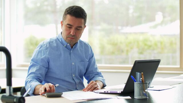 remote job, business and people concept - middle-aged man with calculator, papers and laptop computer working at home office