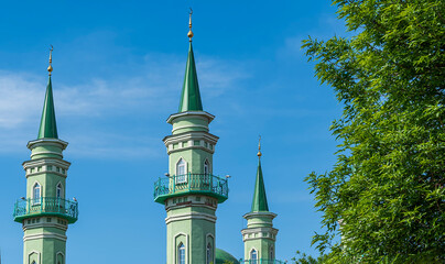 Three green minarets of a Muslim mosque on a background of blue summer sky