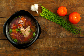 A black dish of vegetable soup with vegetables on a table in the background.