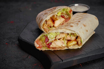 Wrap with fried chicken, vegetables and sauce isolated on dark  background