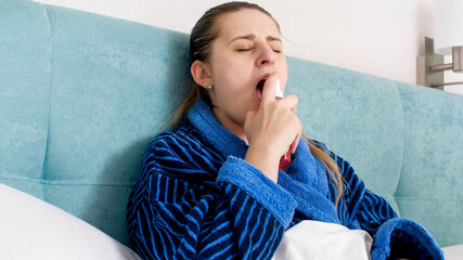 Portrait of sick woman with flu using thpat spray