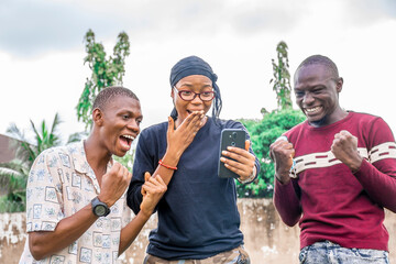 three african friends looking surprised and excited while looking at a mobile phone