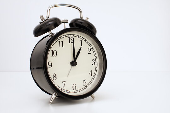 Black vintage alarm clock on table. White background. Wake up concept. An image of a retro clock showing 01:00 pm/am.    
