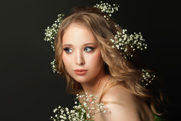 Cheerful woman with long healthy curly hair and white flowers on black background